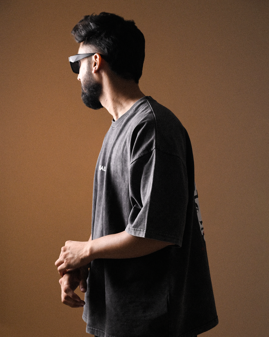 Man wearing a dark t-shirt and sunglasses against a brown background