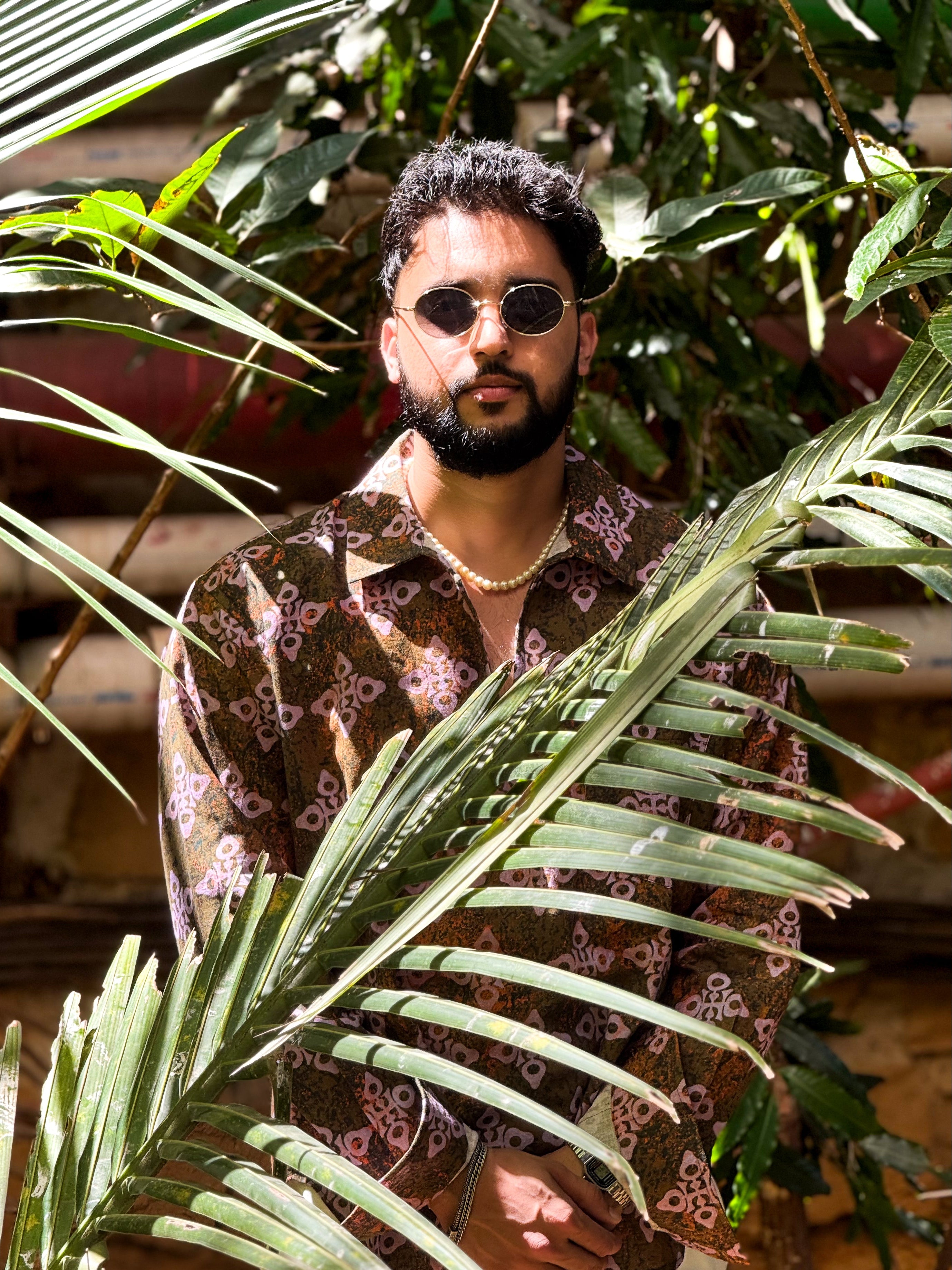 Man wearing sunglasses and a patterned shirt standing among green plants